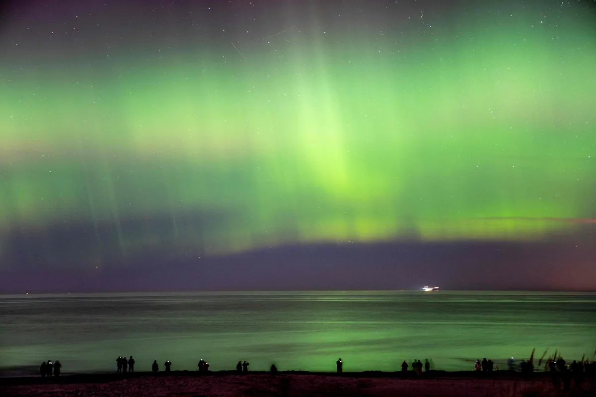 102219536-topshot-northern-lights-aurora-borealis-illuminate-the-sky-as-visitors-walk-along-hornba.j.webp