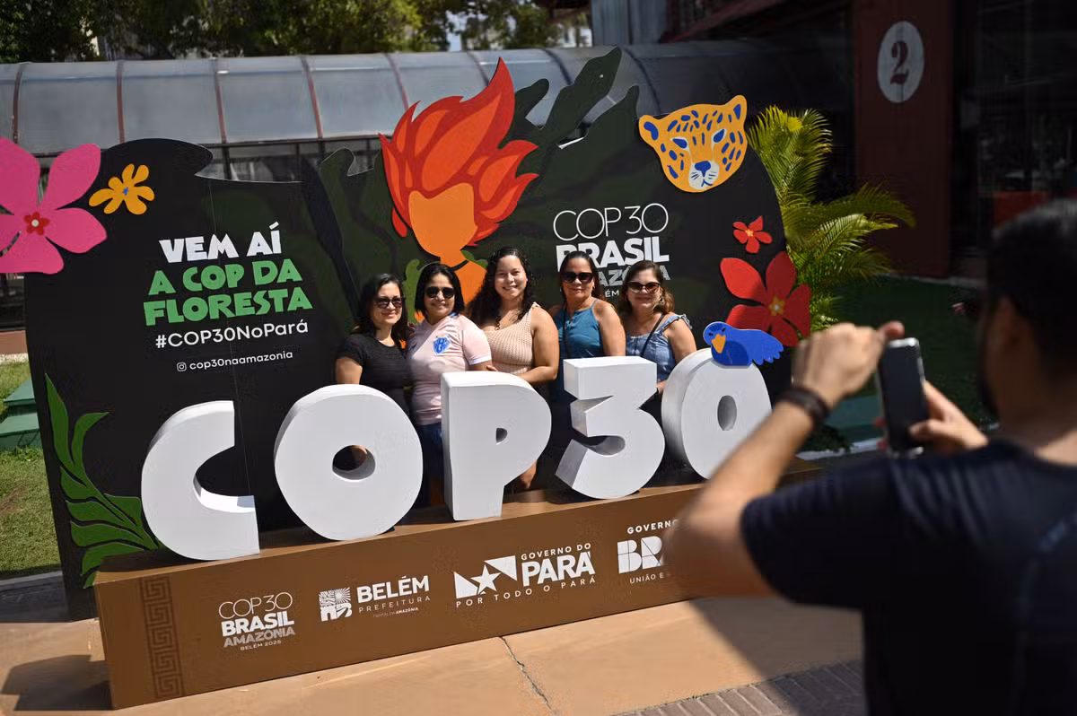 112970345-people-pose-for-a-picture-with-a-banner-of-the-cop30-inside-the-estacao-das-docas-a-touris.avif