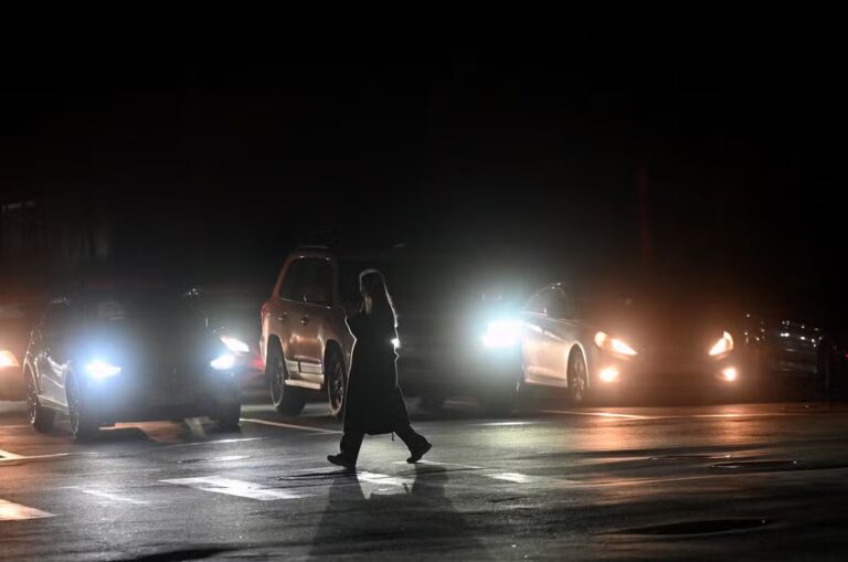 112997122-a-girl-walking-by-the-pedestrian-way-is-lit-by-car-headlights-during-blackout-hours-in-kyi.avif