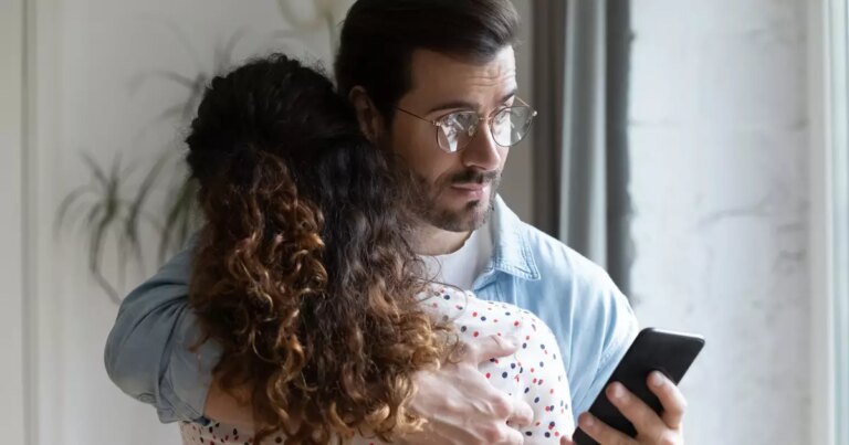 705375487-homem-olhando-o-celular-enquanto-abraca-a-esposa-orig-1.jpg