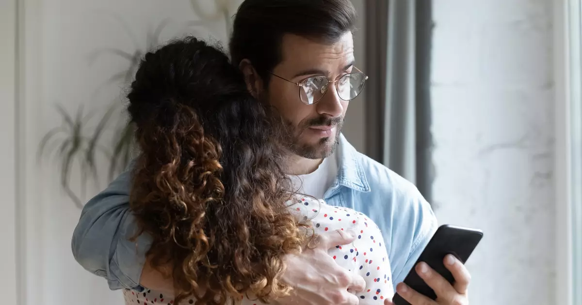 705375487-homem-olhando-o-celular-enquanto-abraca-a-esposa-orig-1.jpg
