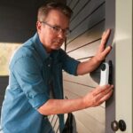 A man installs a wired model of the Google Nest Doorbell near his front door.